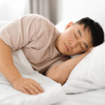 Tired middle aged asian man asleep, resting peacefully in bed